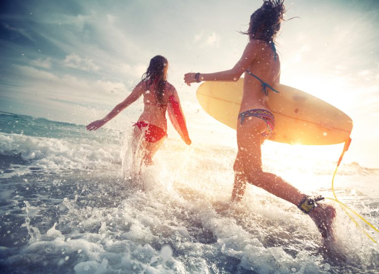 Two,Young,Ladies,Surfers,Running,Into,The,Sea,With,Surf