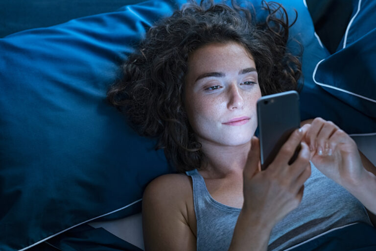 Top,View,Of,Young,Woman,Using,A,Smartphone,While,Lying